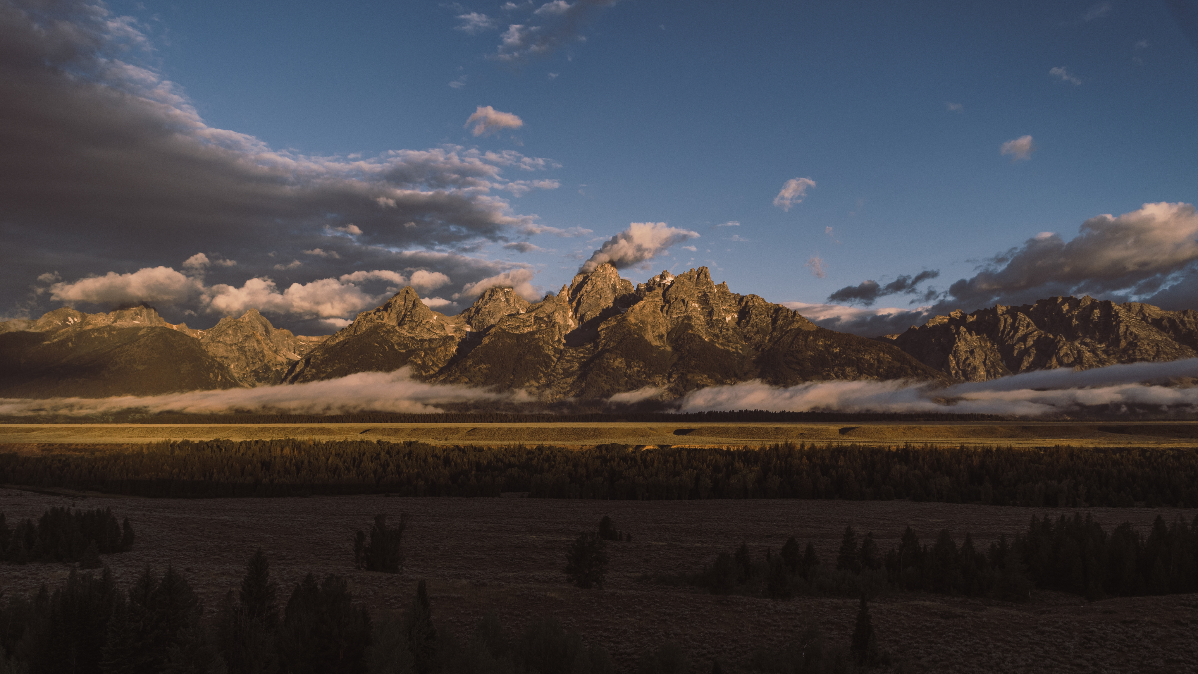 A picture of Sunrise at Grand Teton Mountains with some clouds on the right.